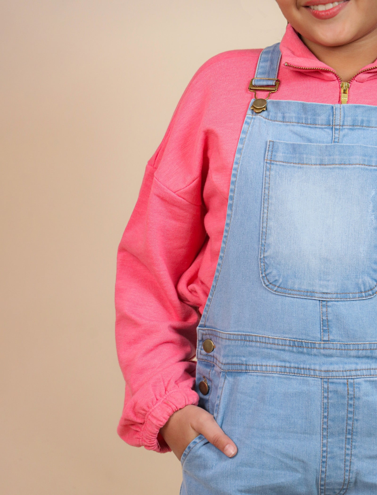 Girls wearing a pink shirt and blue denim overalls on a beige background