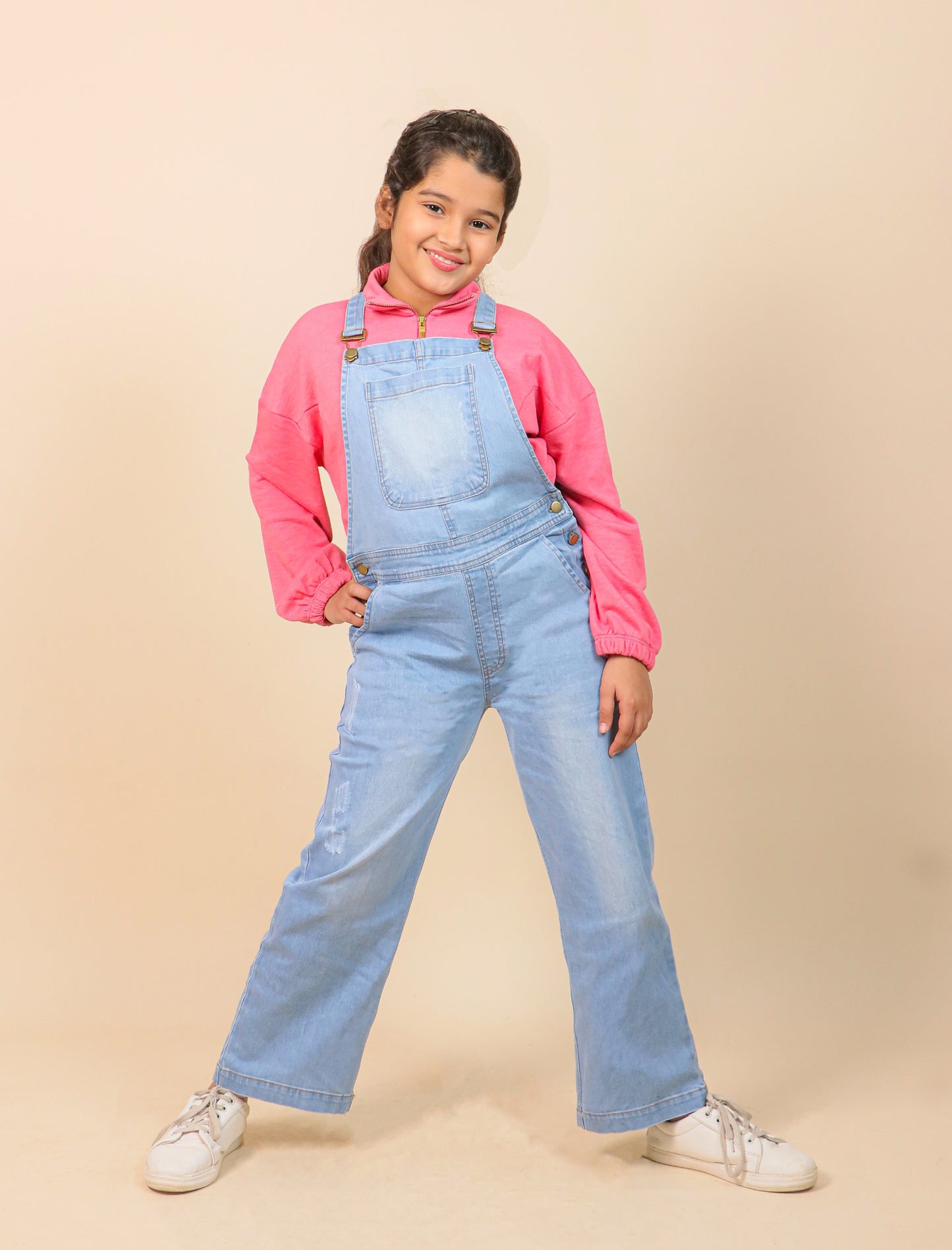 Girls wearing a pink hoodie and blue denim overalls on a beige background