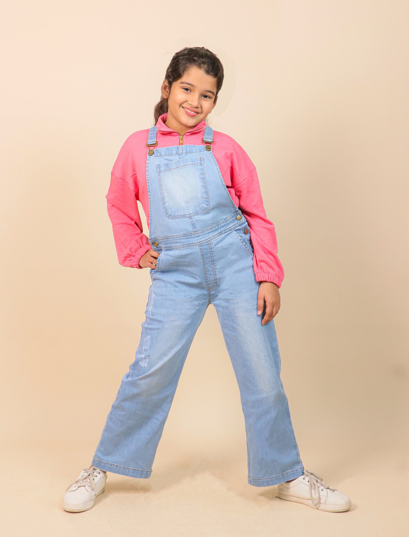 Girls wearing a pink hoodie and blue denim overalls on a beige background