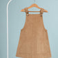 Brown suede pinafore dress on a hanger against a light blue background