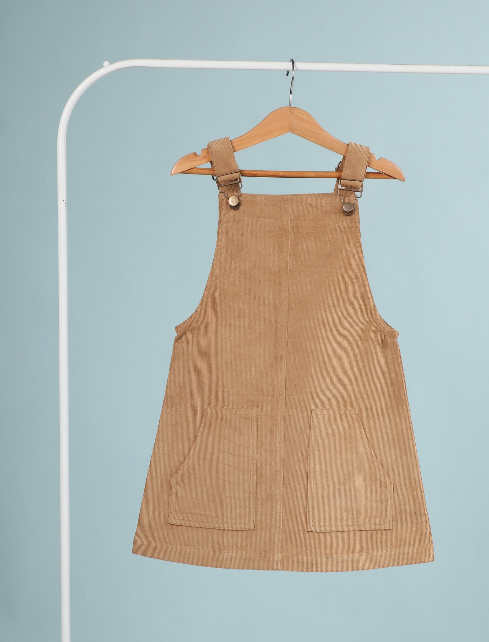 Brown suede pinafore dress on a hanger against a light blue background