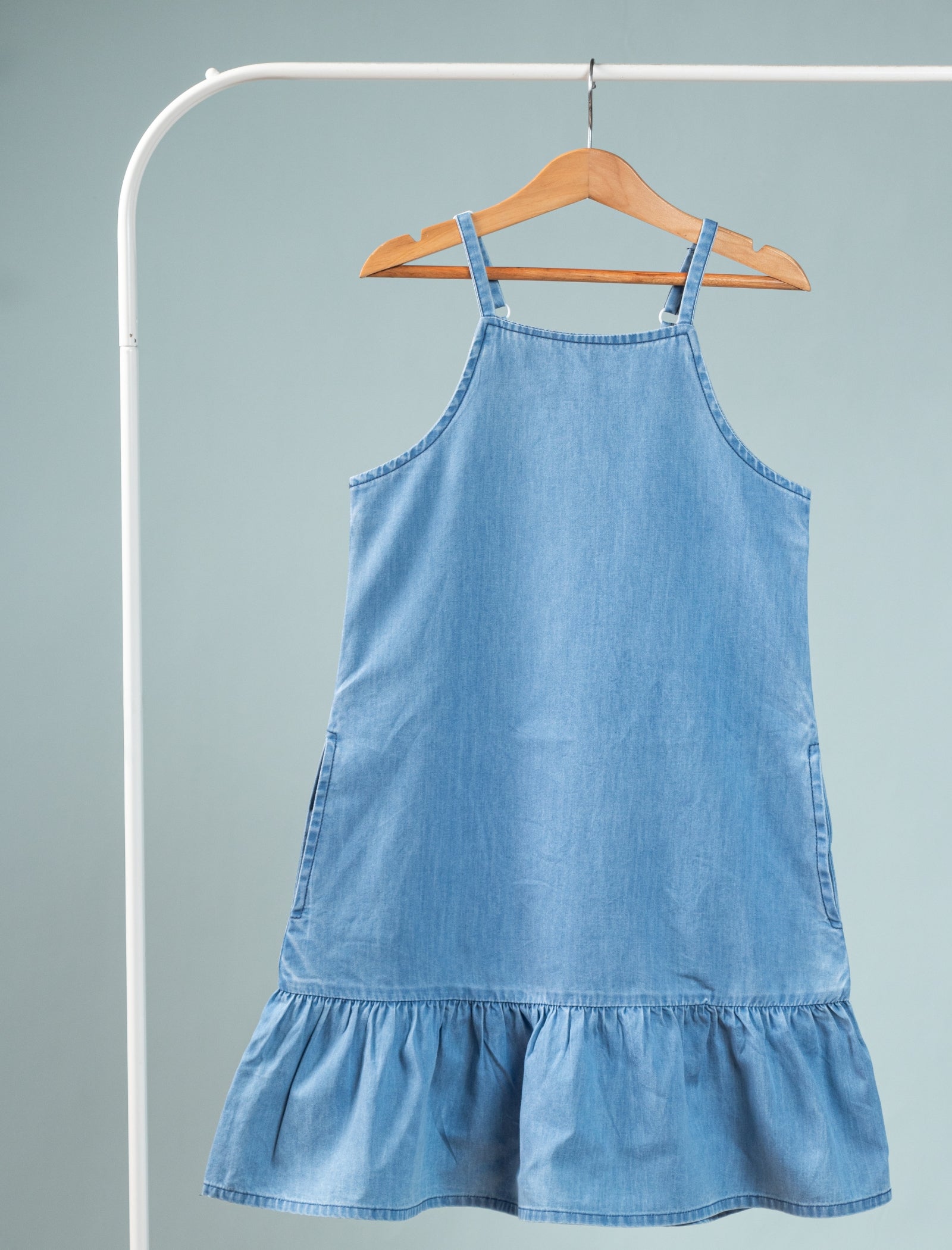 Blue denim dress on a hanger against a gray background