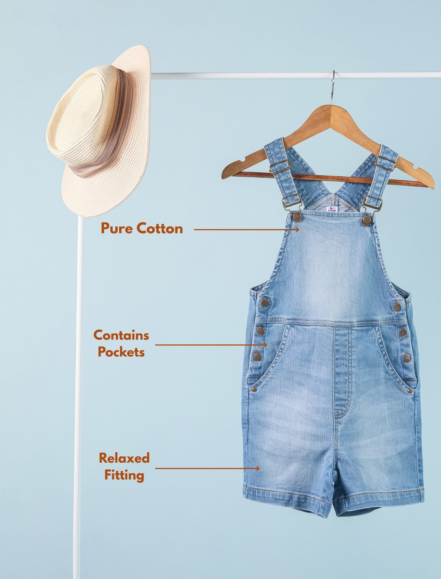 Blue denim overalls on a hanger with a straw hat on a stand against a light blue background.