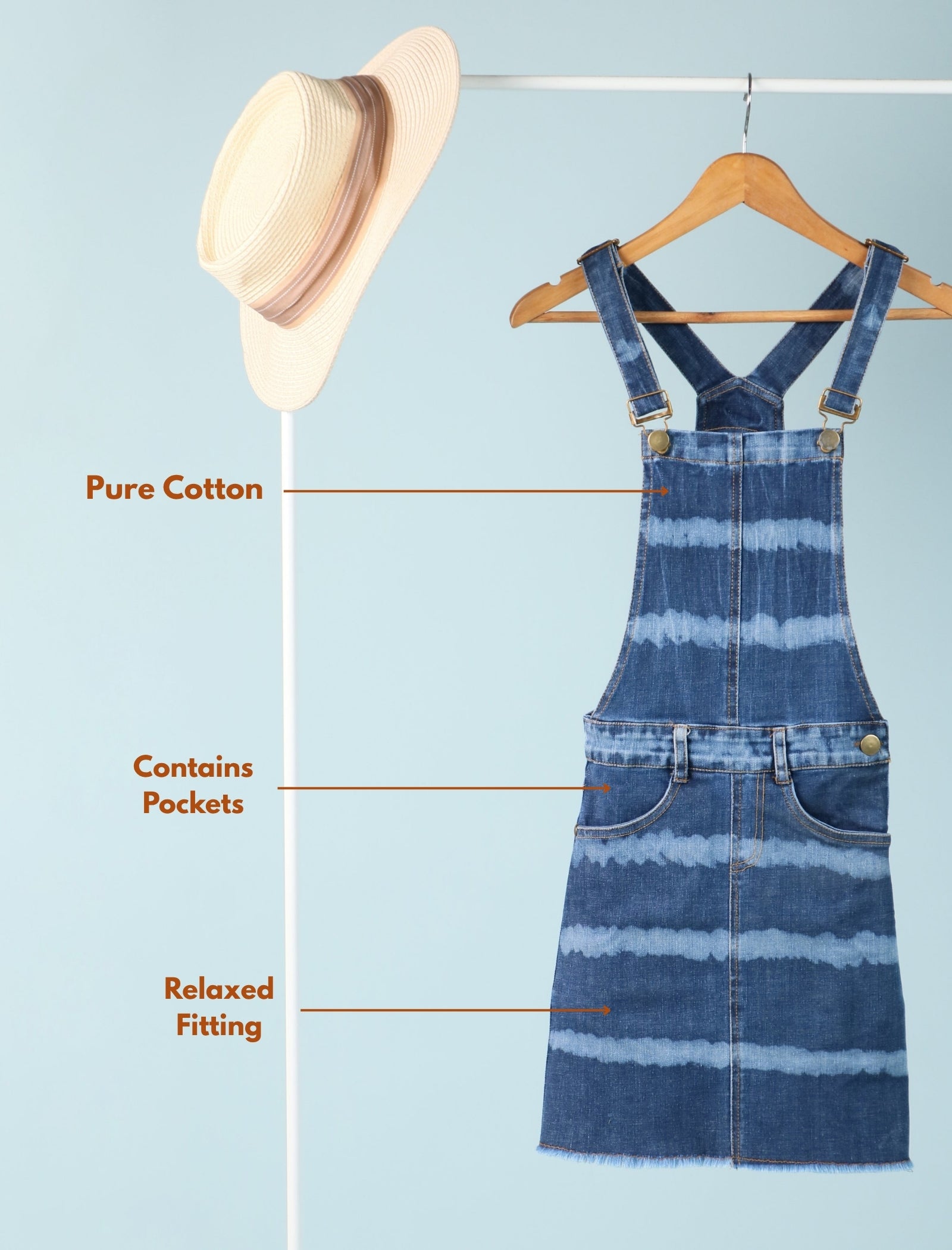 Striped denim dress on a hanger with a hat next to it on a light blue background