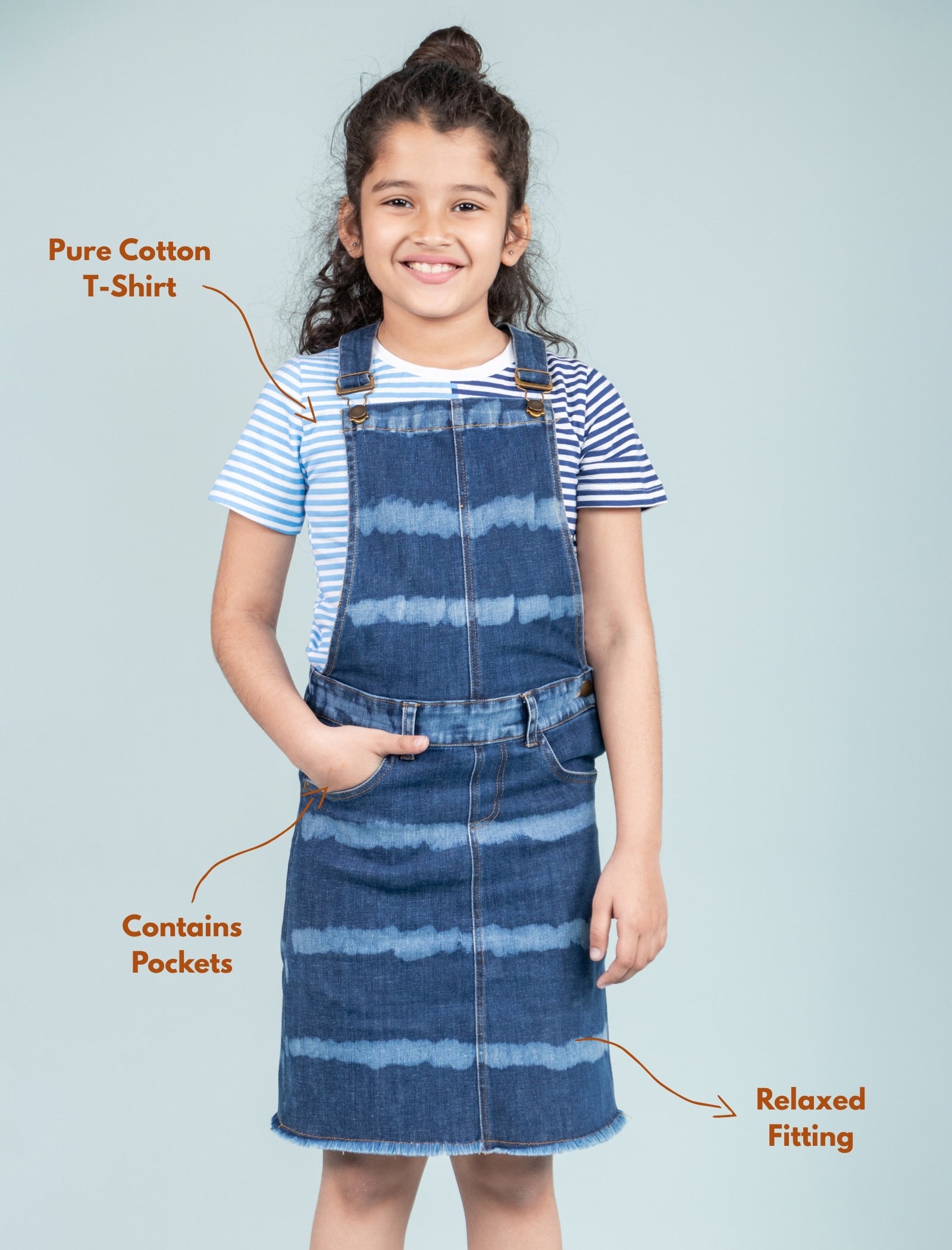 Girl wearing a denim dress over a striped shirt with text highlighting features on a light blue background