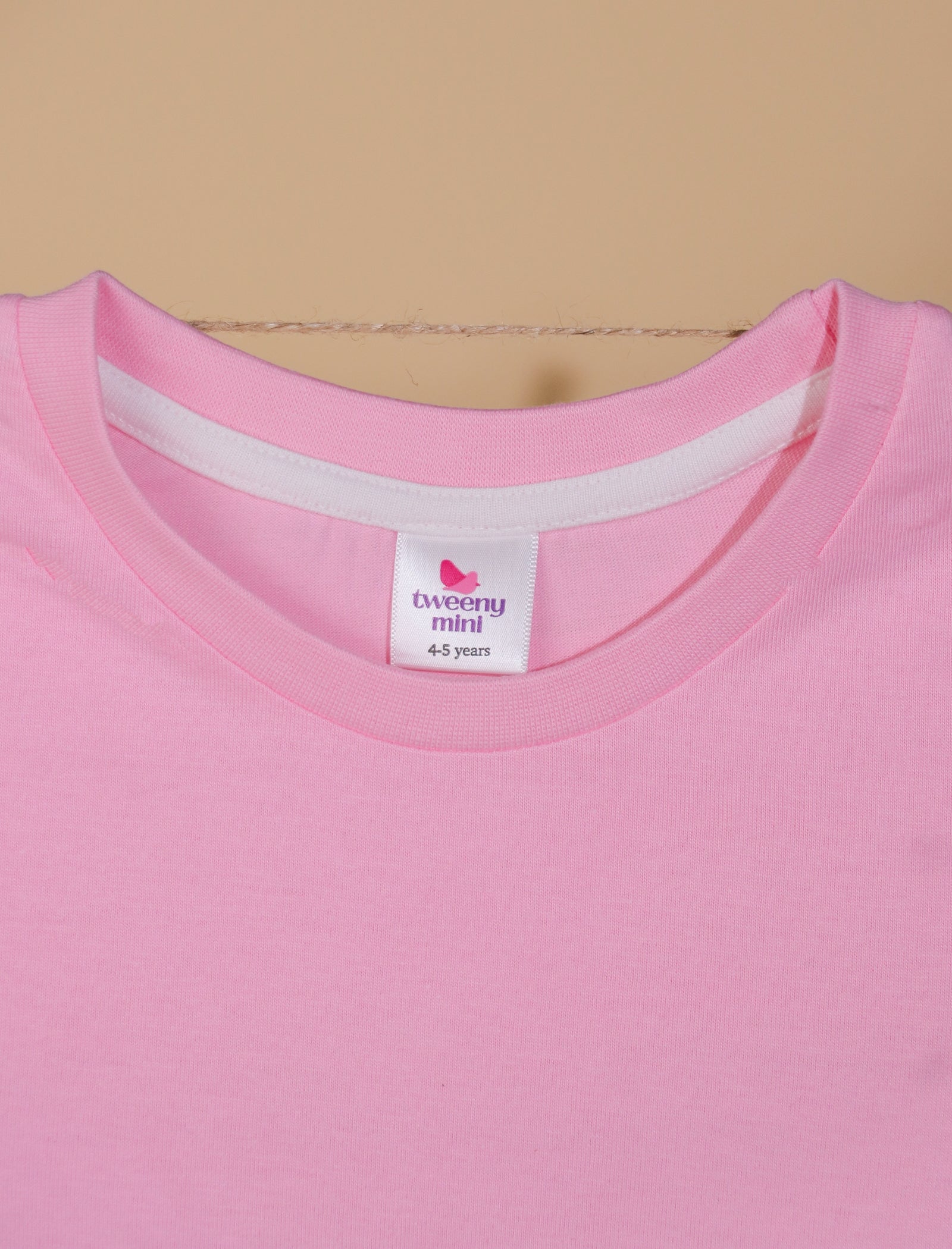 Close-up of a pink t-shirt with a brand label on a beige background