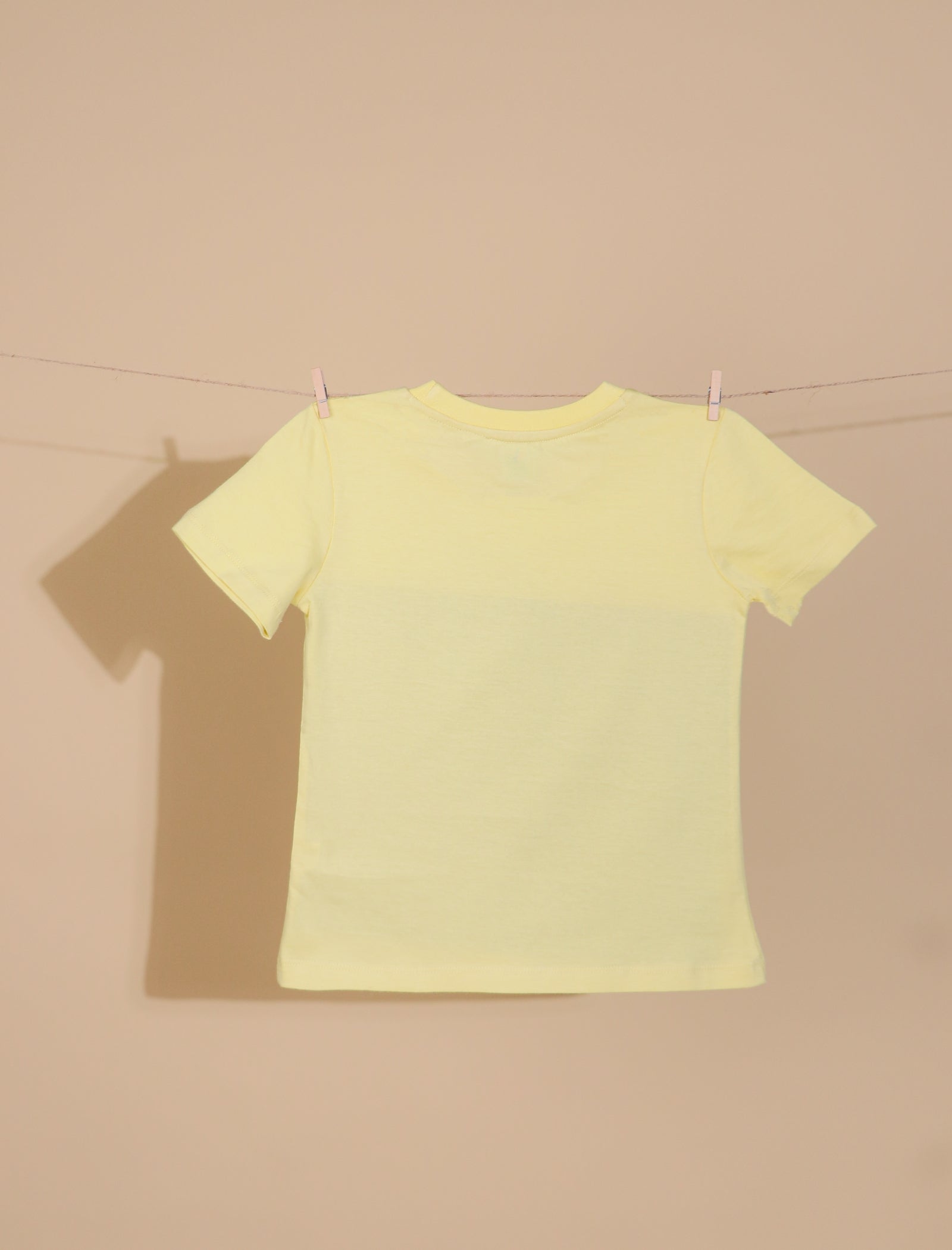 Yellow t-shirt on a clothesline against a beige wall