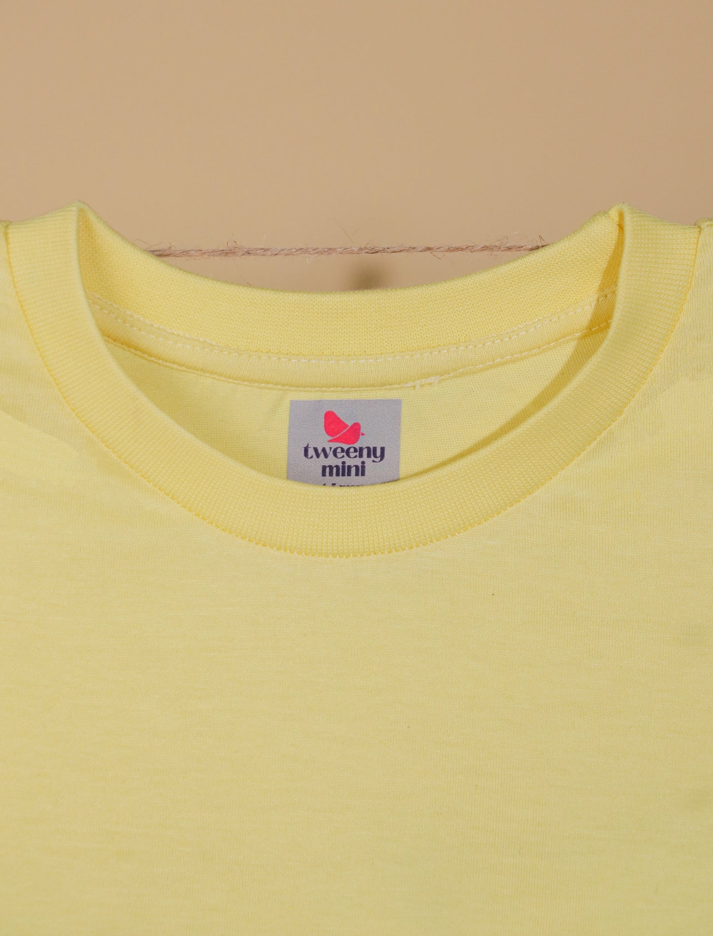 Yellow t-shirt with a brand label on a beige background
