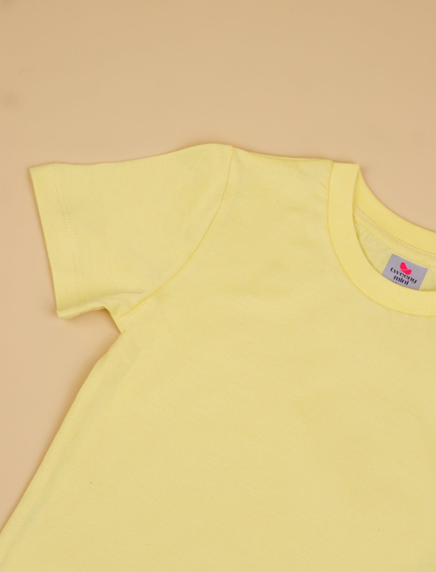 Yellow t-shirt with a brand label on a beige background