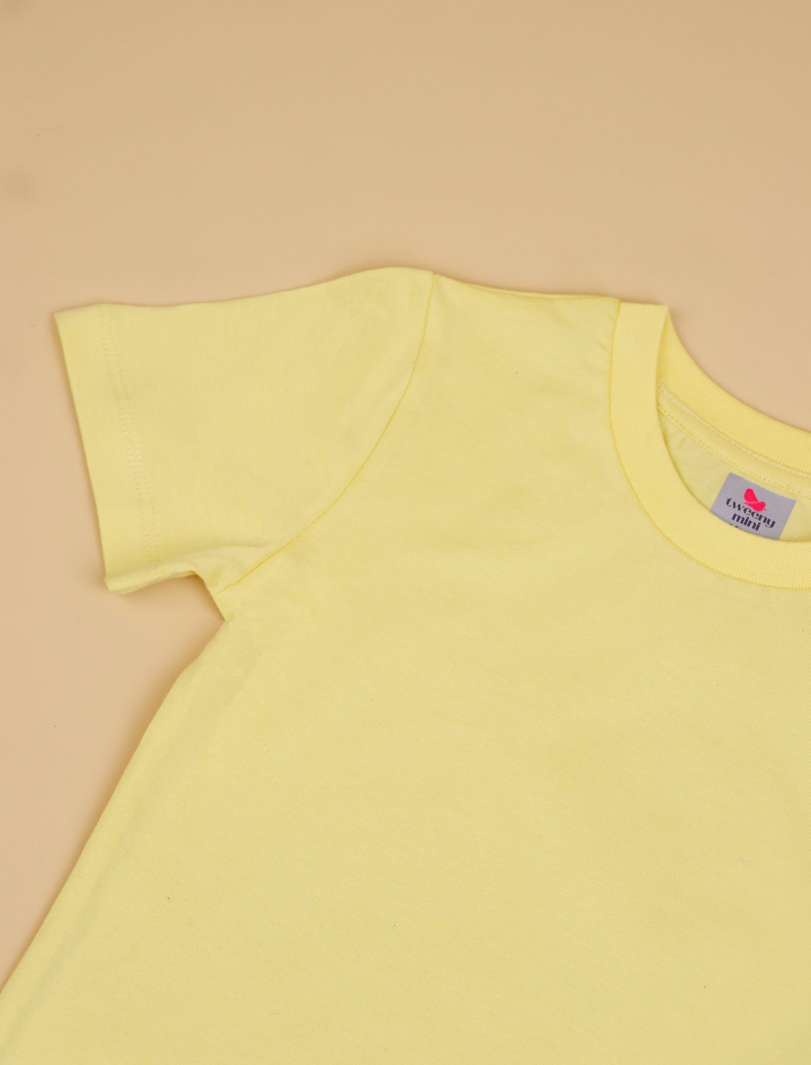 Yellow t-shirt with a brand label on a beige background