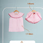 Pink children's outfit with t-shirt and shorts on hangers against a gray background.