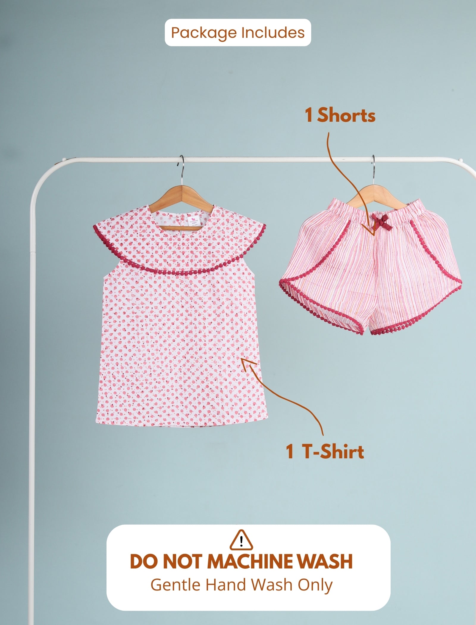 Pink children's outfit with t-shirt and shorts on hangers against a gray background.