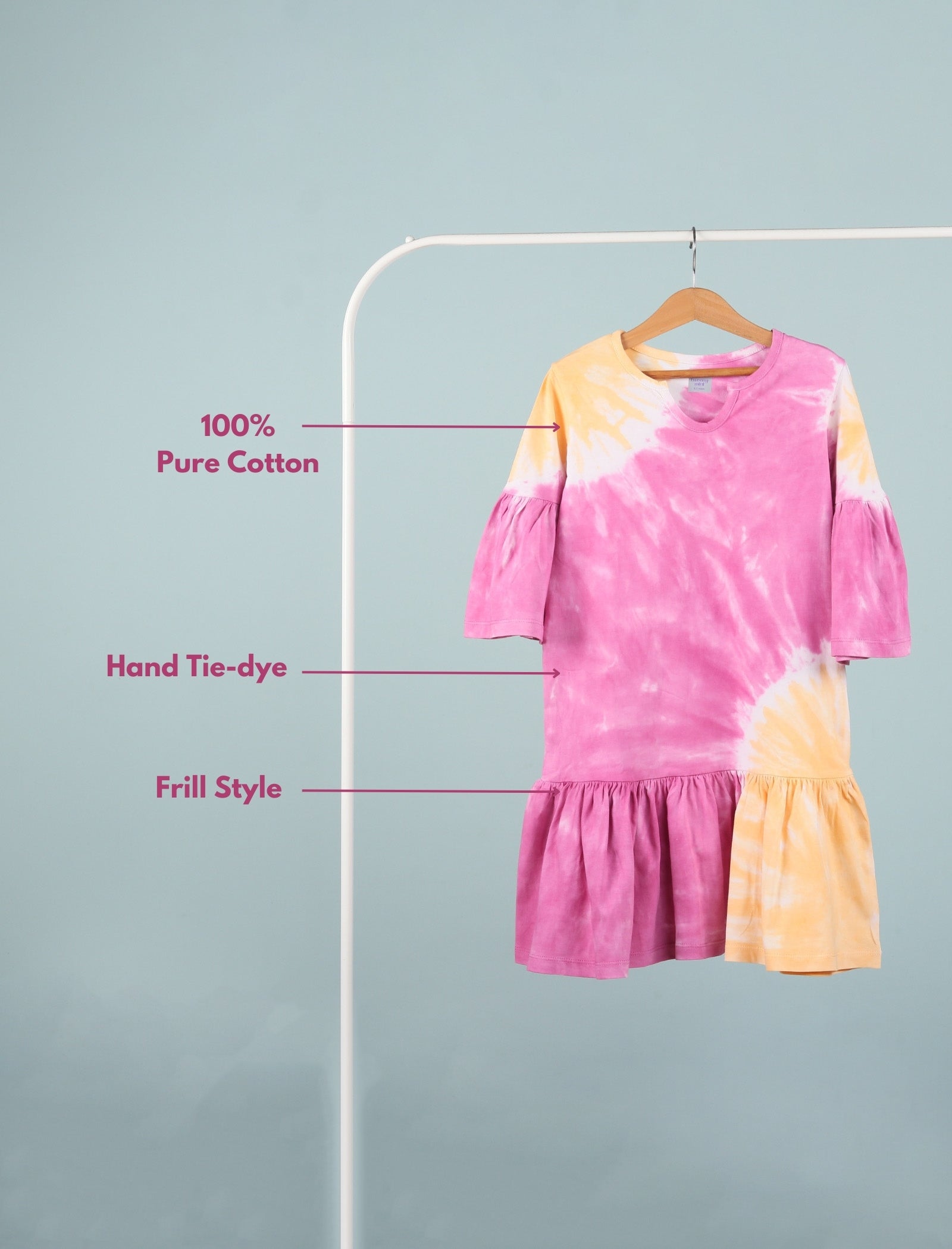 Tie-dye dress with pink and yellow colors on a hanger against a gray background.