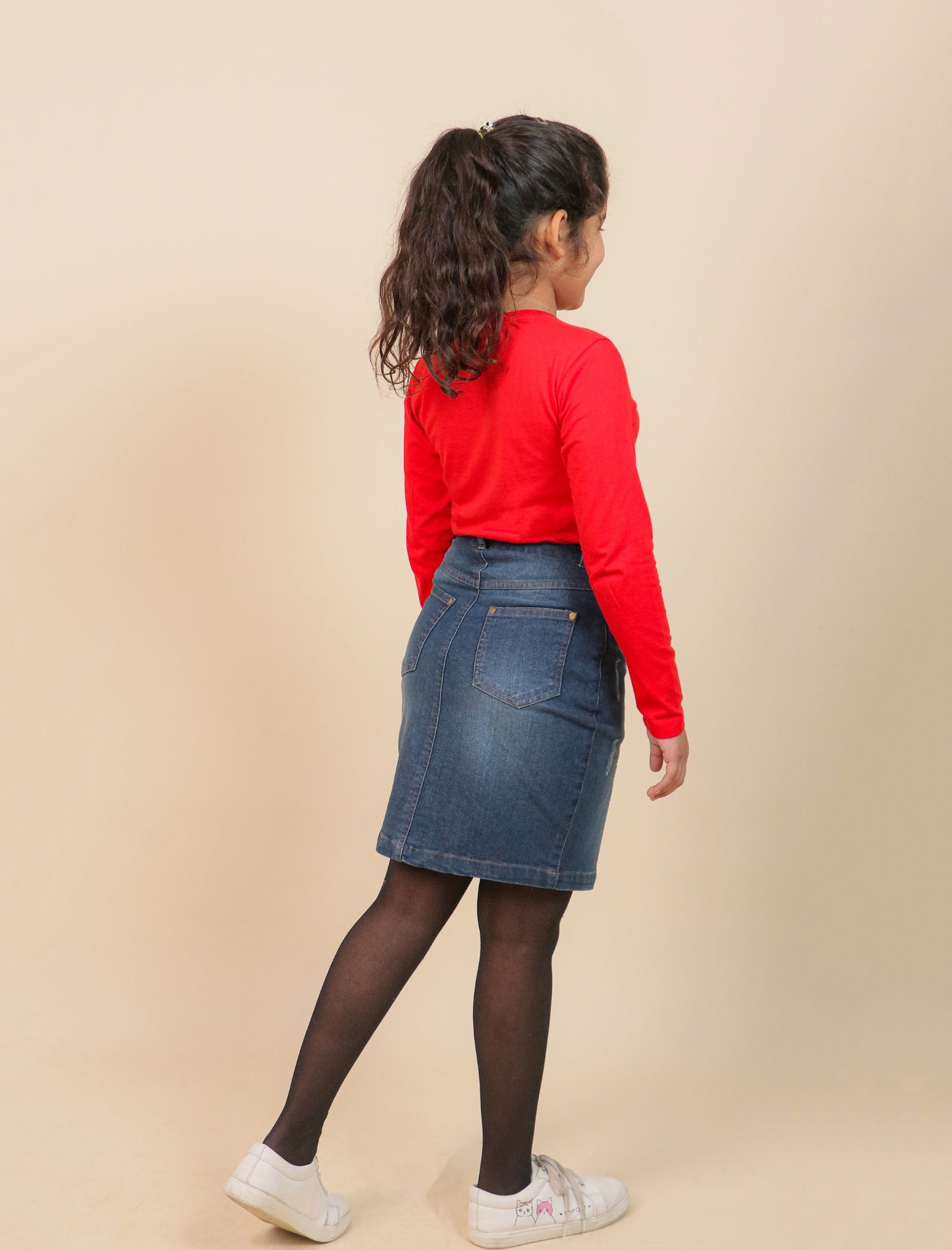 Girls wearing a red sweater and blue denim skirt on a beige background