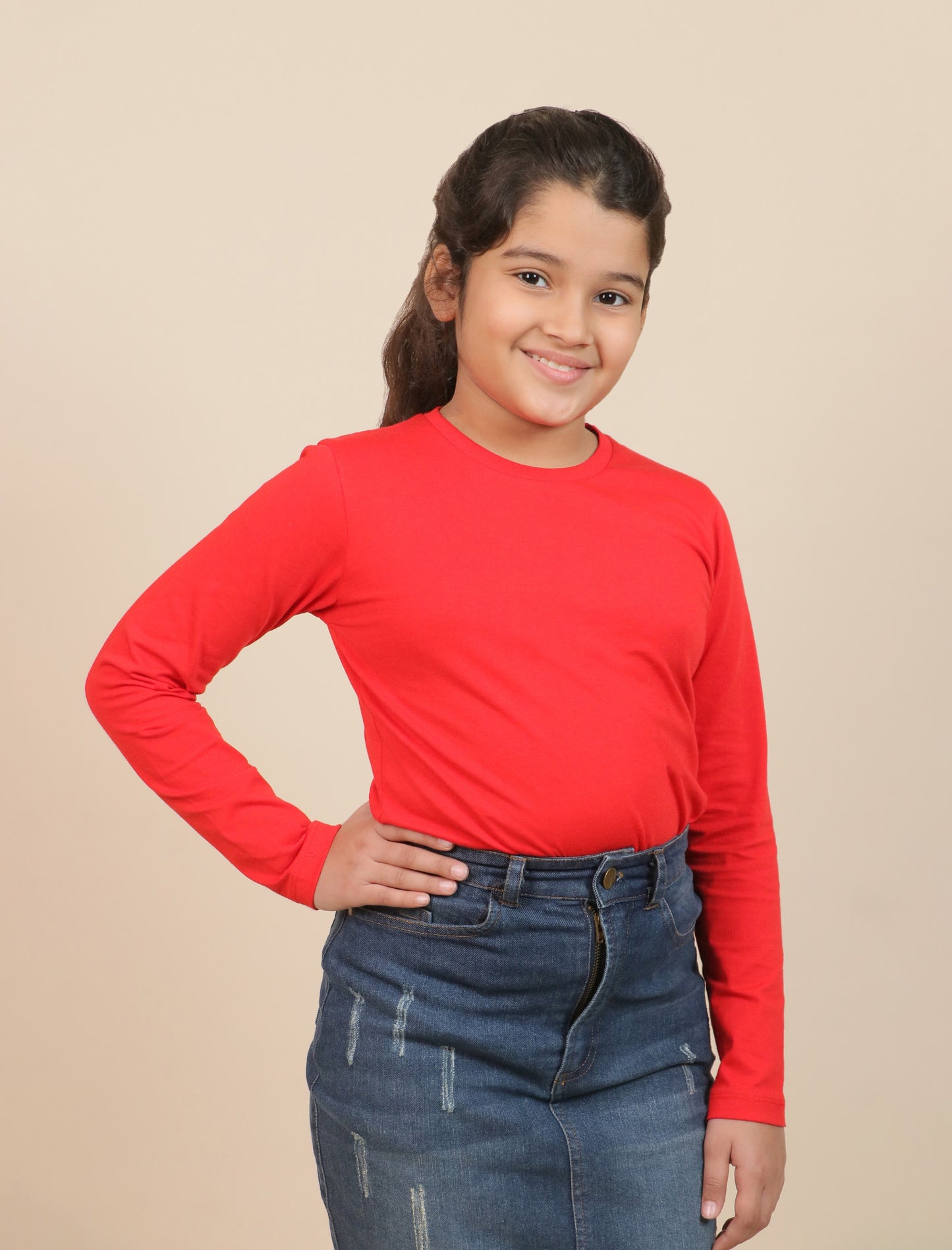 girl wearing a red long-sleeve shirt and blue jeans on a beige background