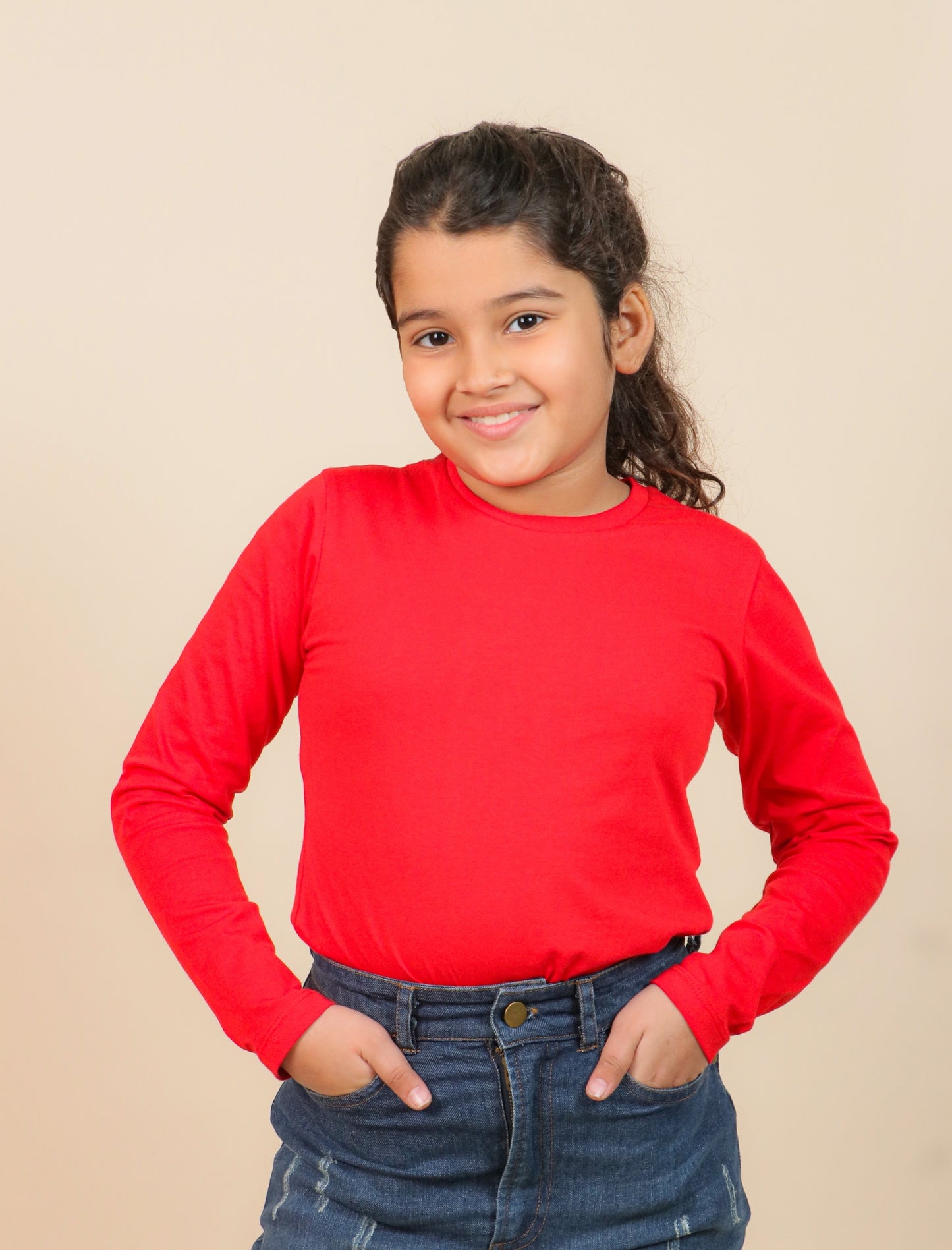 Girls wearing a red long-sleeve shirt and blue jeans against a beige background