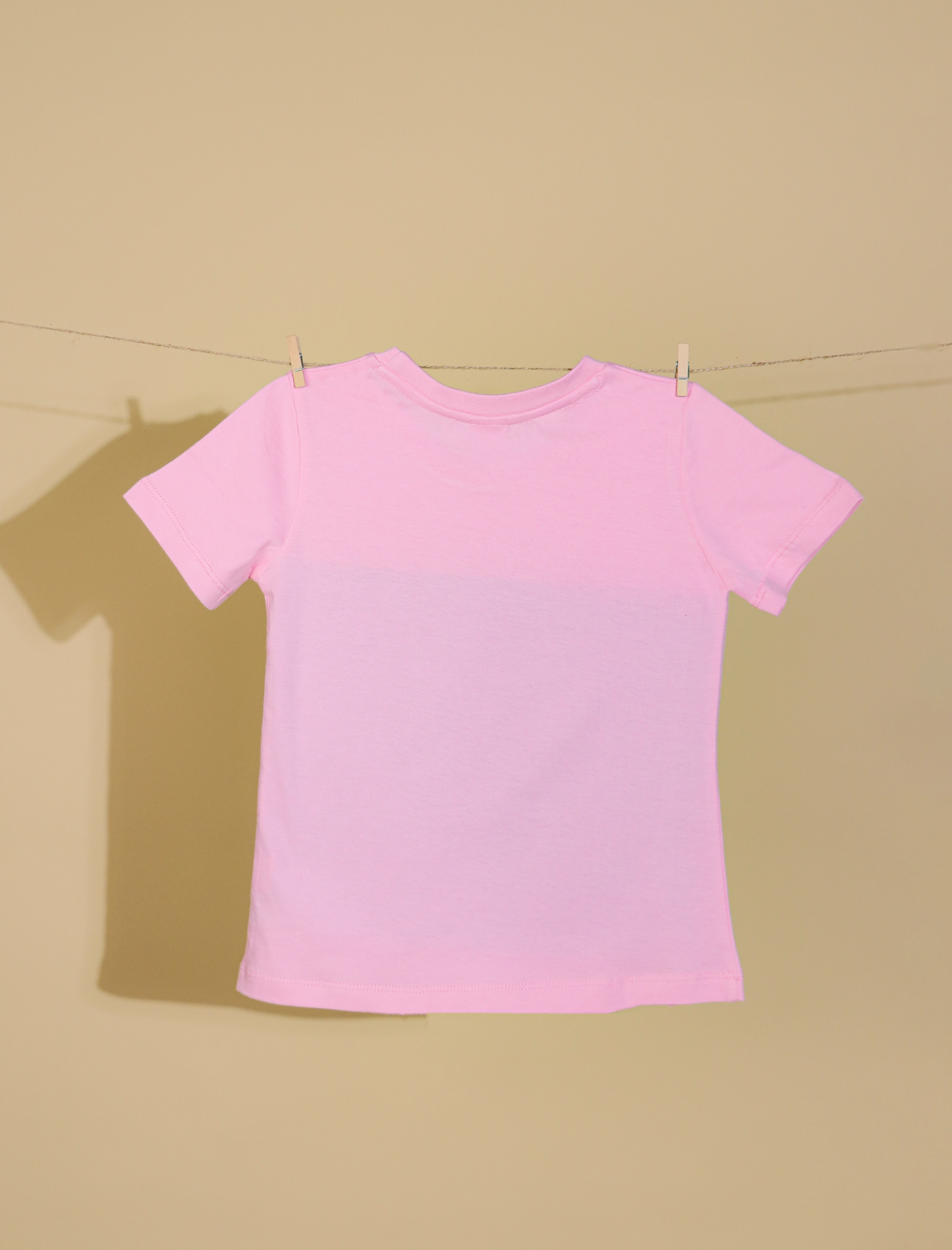 Pink t-shirt on a clothesline against a beige background