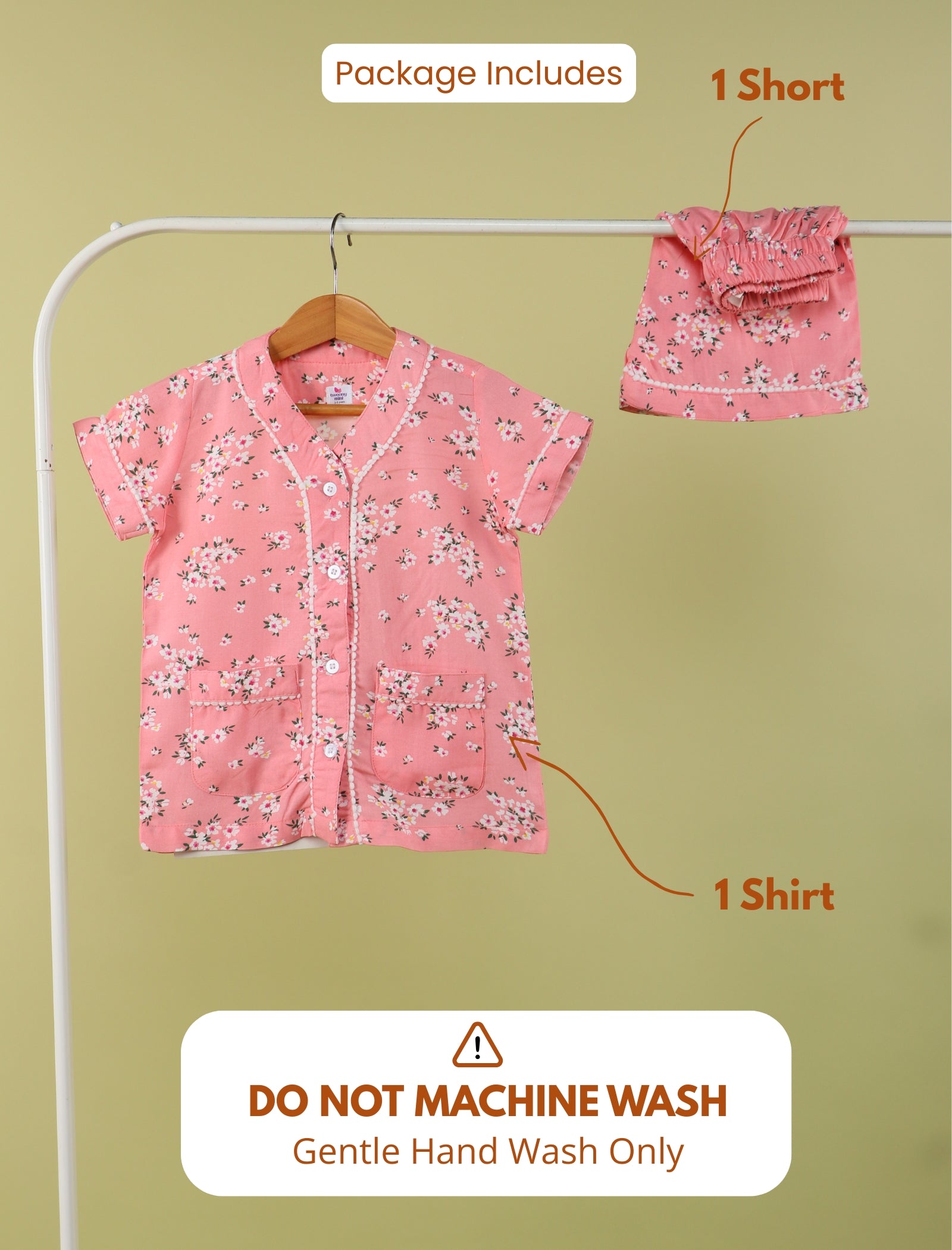 Pink girls outfit with shirt and shorts on a hanger against a green background.