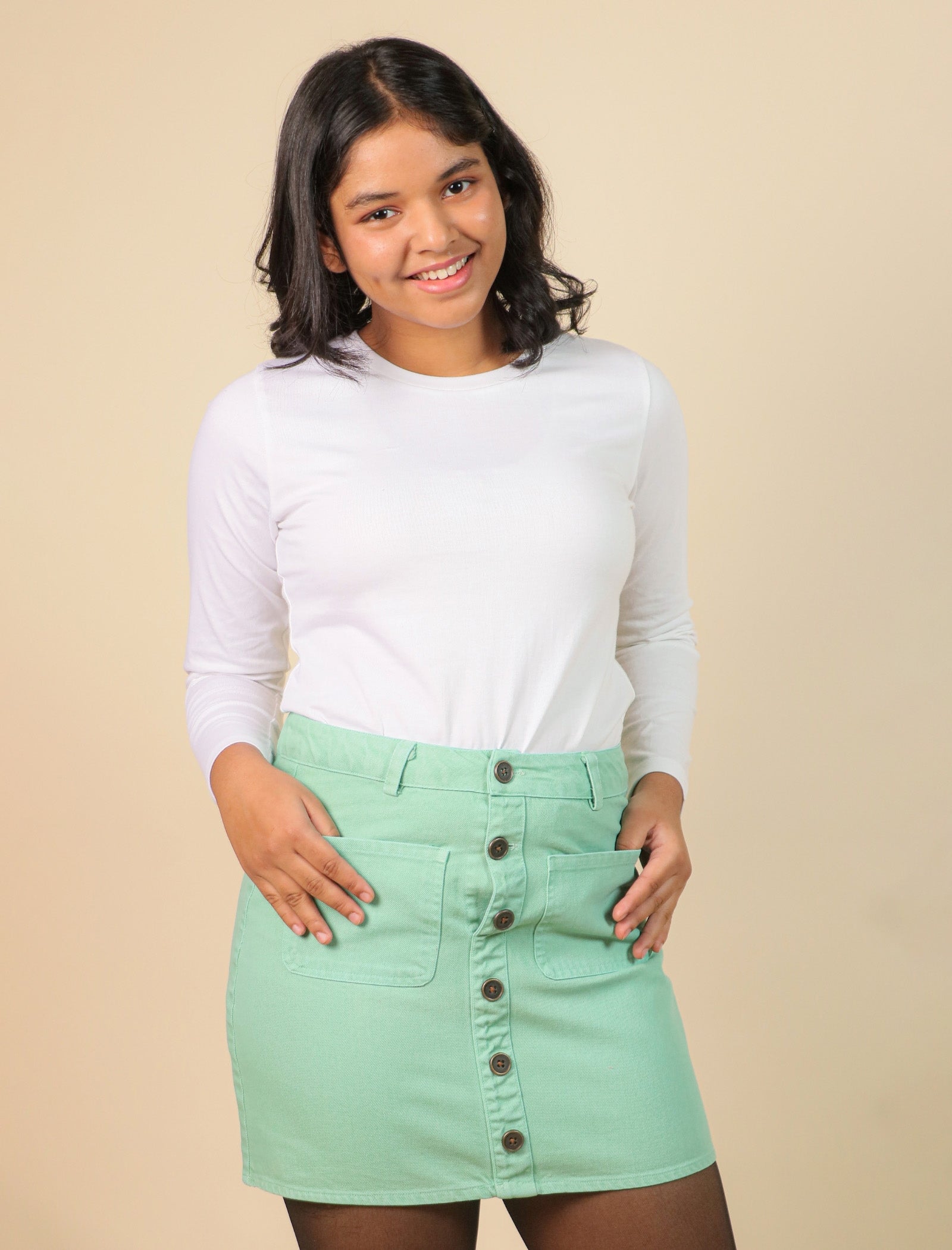 girls wearing a white long-sleeve shirt and light green skirt against a beige background