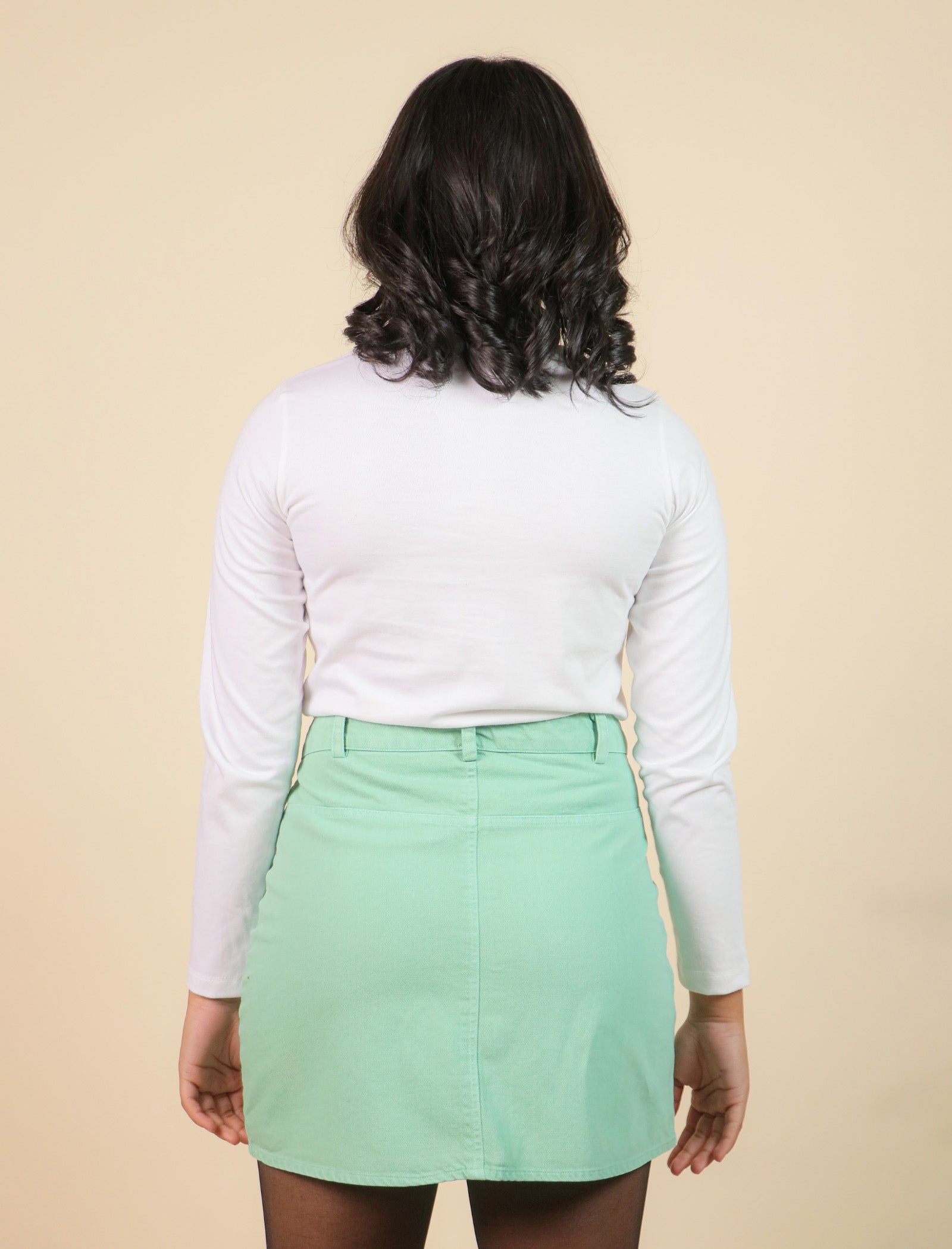 Girls wearing a white long-sleeve shirt and light green skirt on a beige background