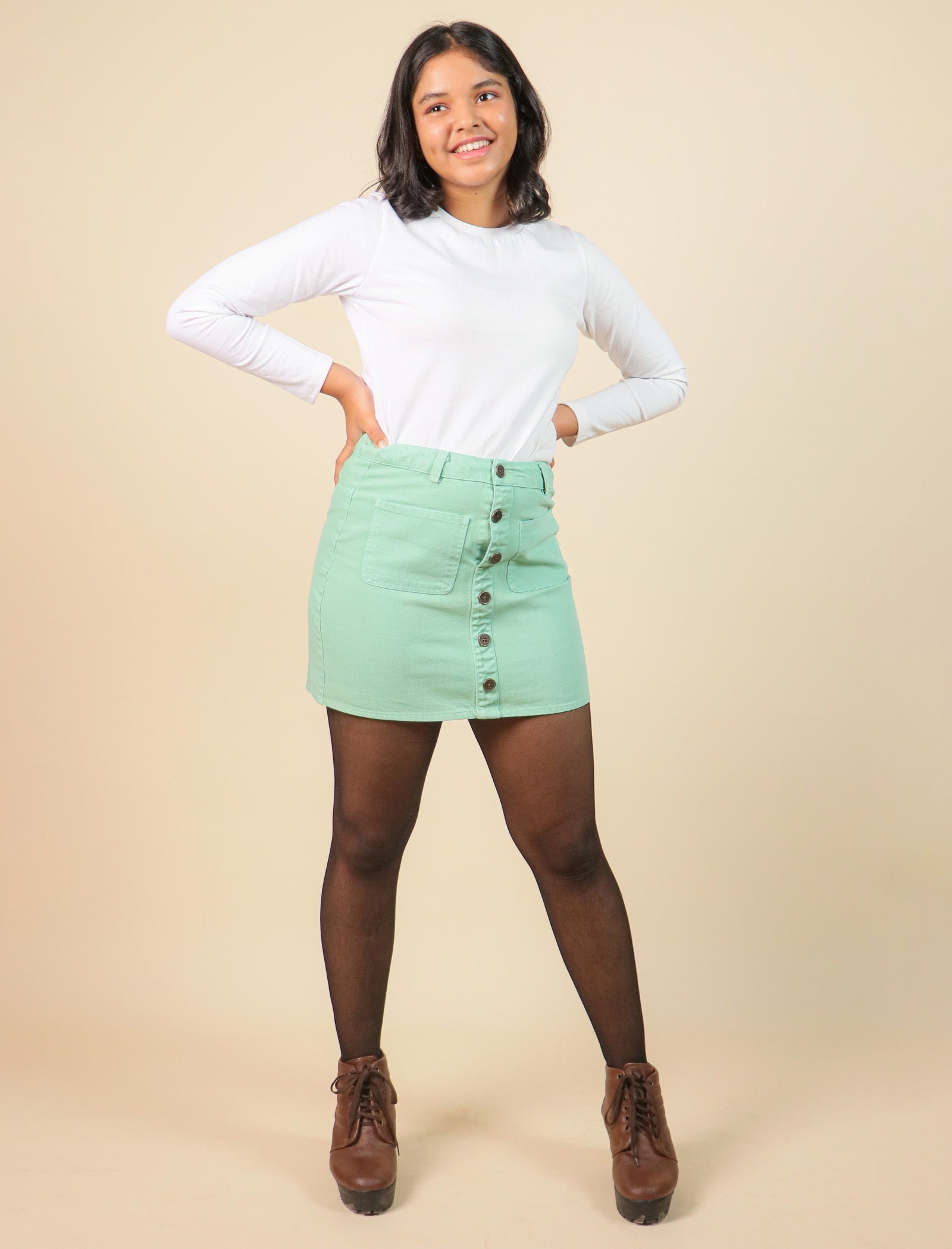 Girls wearing a white long-sleeve top and green denim skirt with buttons on a beige background