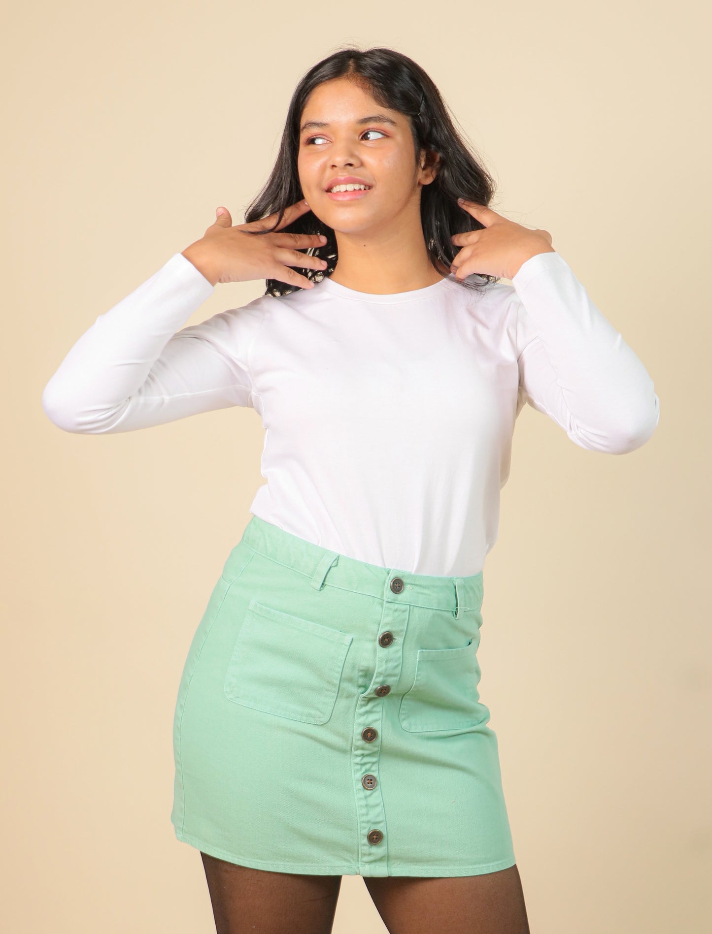 Girls wearing a white long-sleeve top and green skirt against a beige background