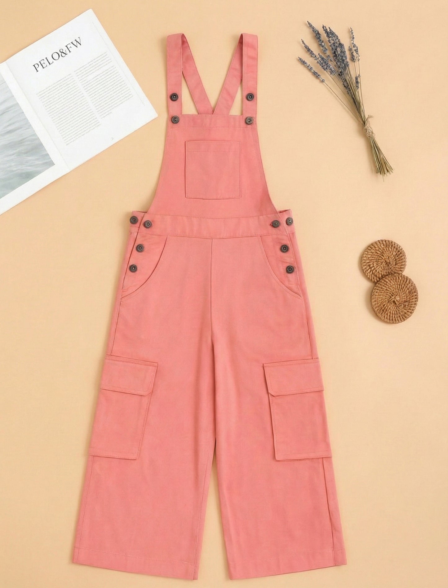 Peach denim overalls on a beige background with a magazine and decorative items.