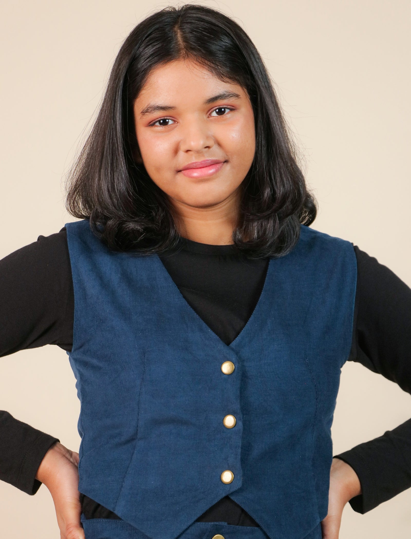Girls wearing a blue vest with gold buttons on a beige background