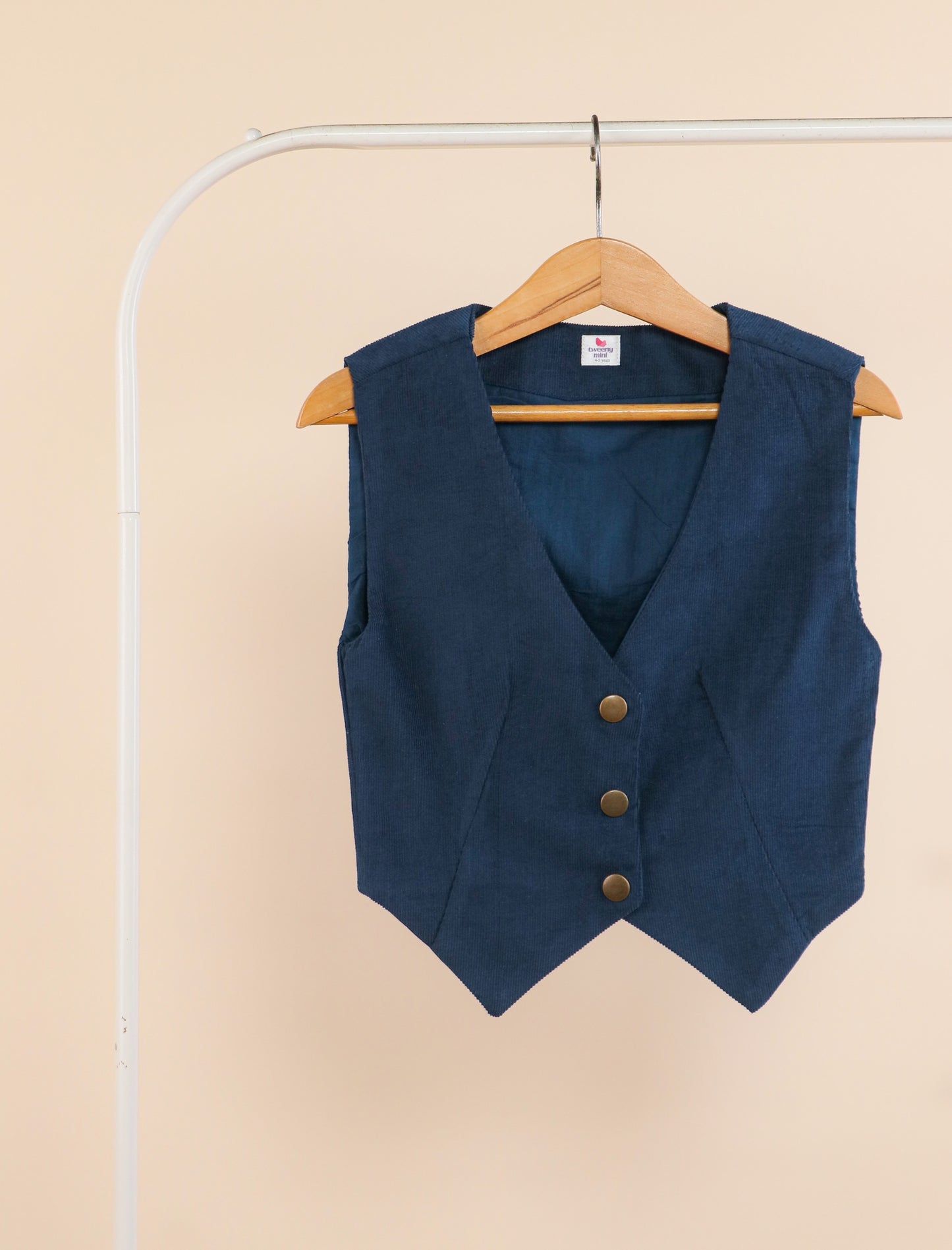 Blue vest with brown buttons on a hanger against a beige background