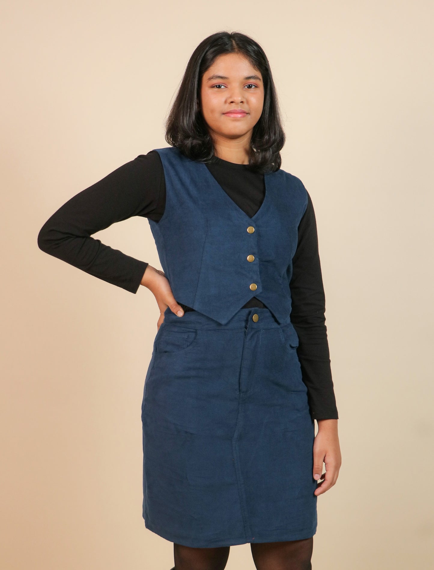 Girls wearing a blue corduroy dress over a black top on a beige background
