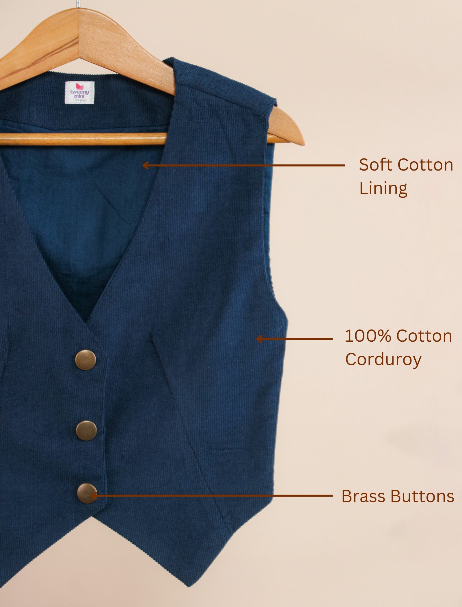Blue vest with labels indicating soft cotton lining, 100% cotton corduroy, and brass buttons on a beige background.