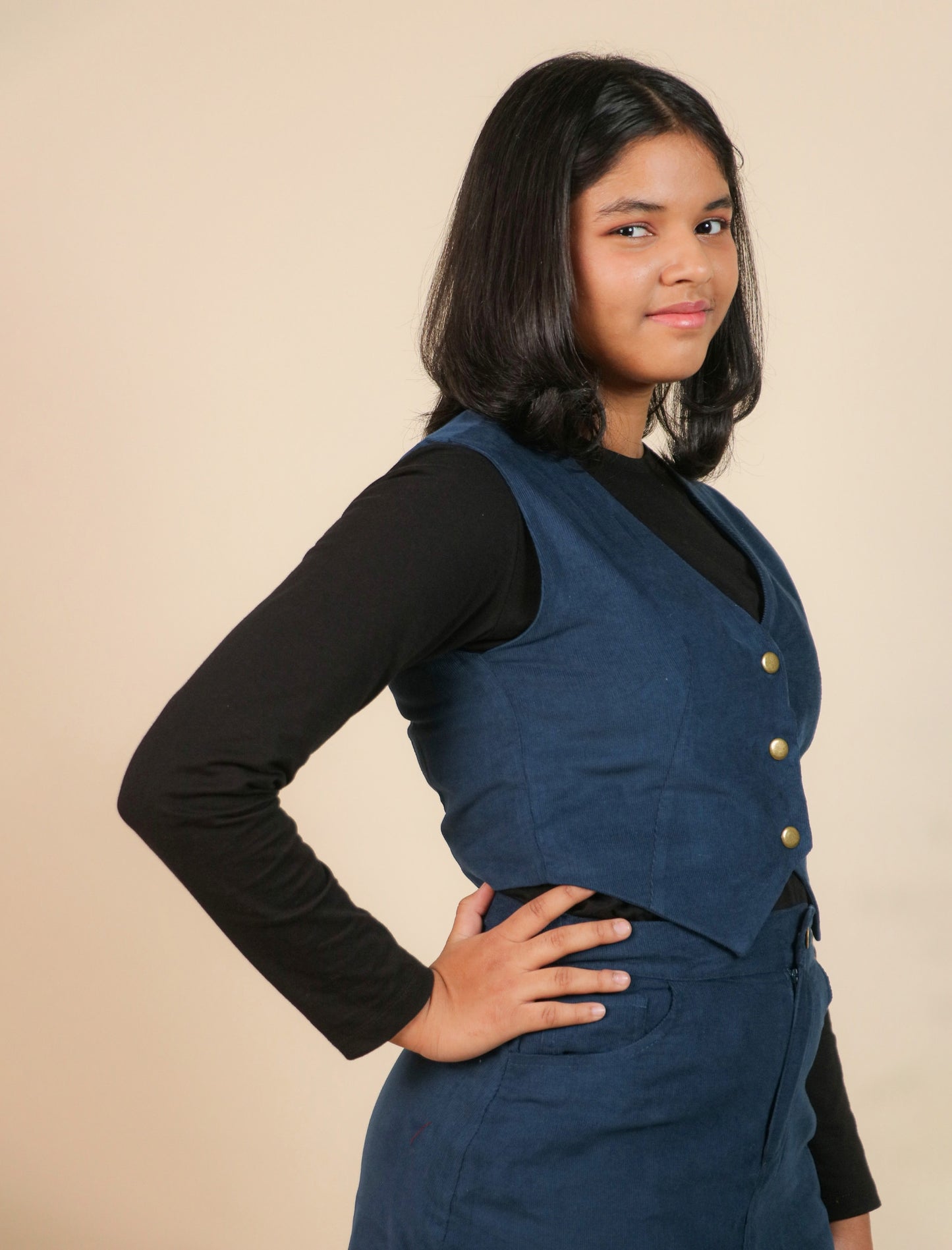 Girls wearing a blue vest over a black shirt on a beige background
