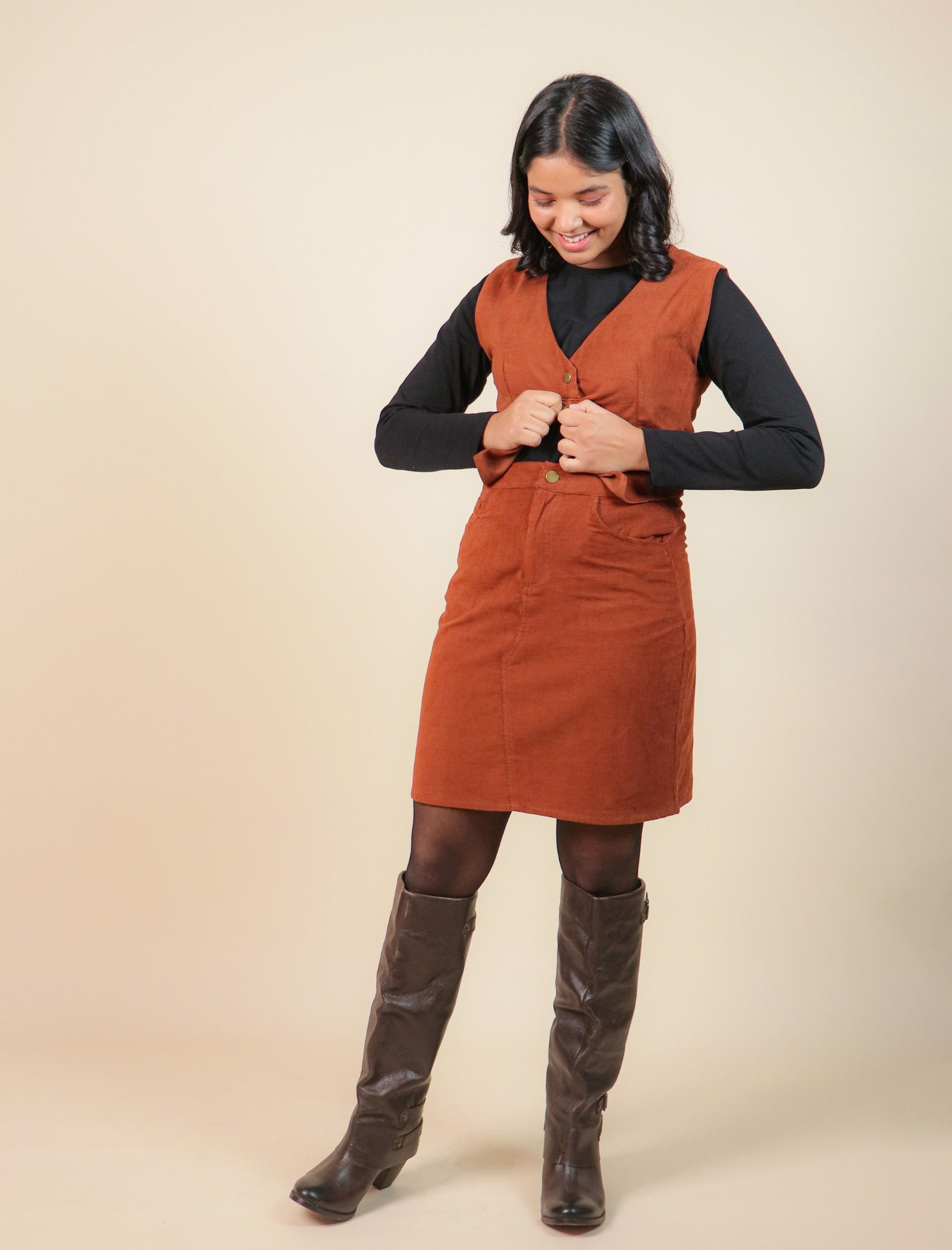 Girls wearing a brown corduroy dress with a black top and brown knee-high boots on a beige background
