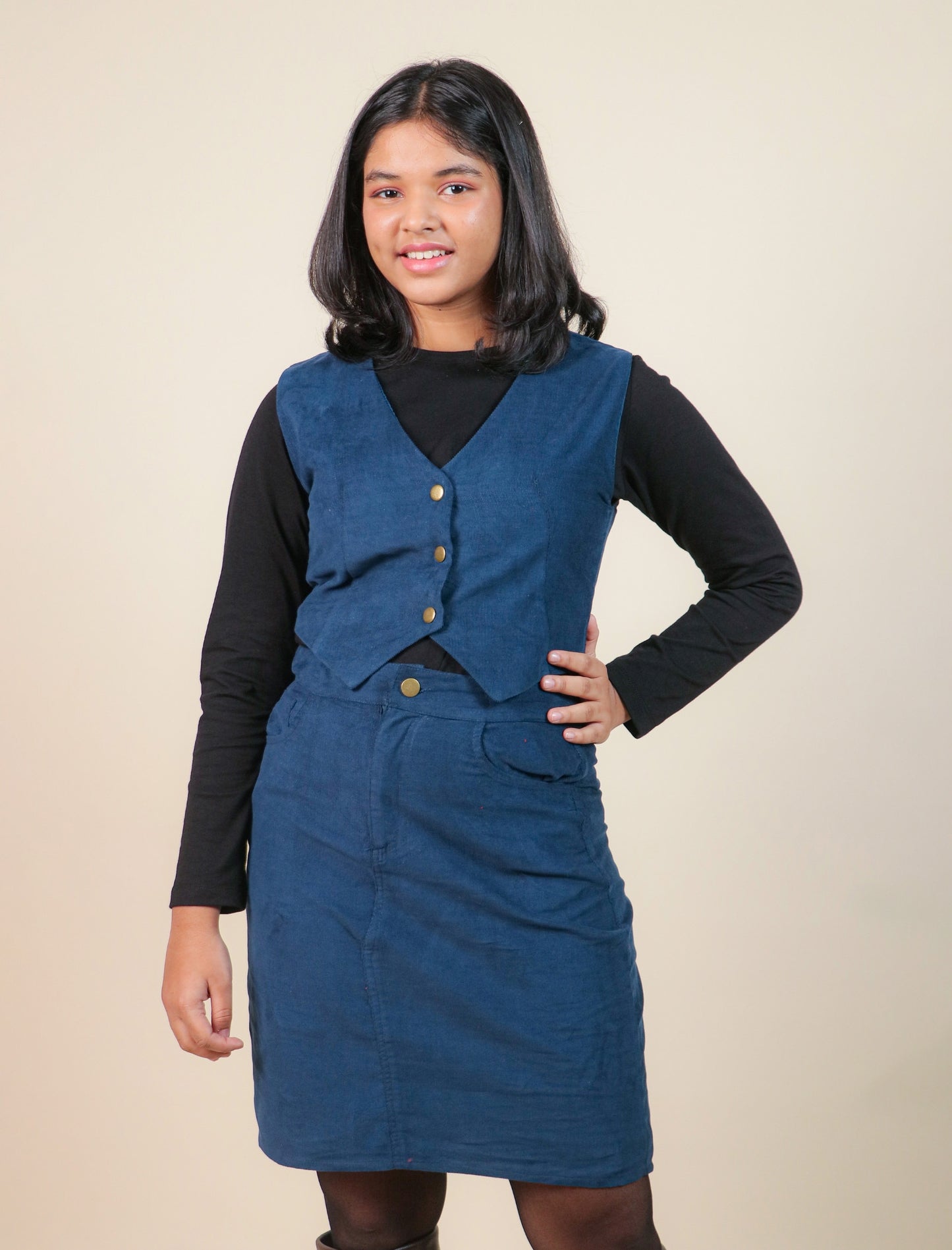 Girl wearing a blue dress with a vest over a black shirt on a beige background