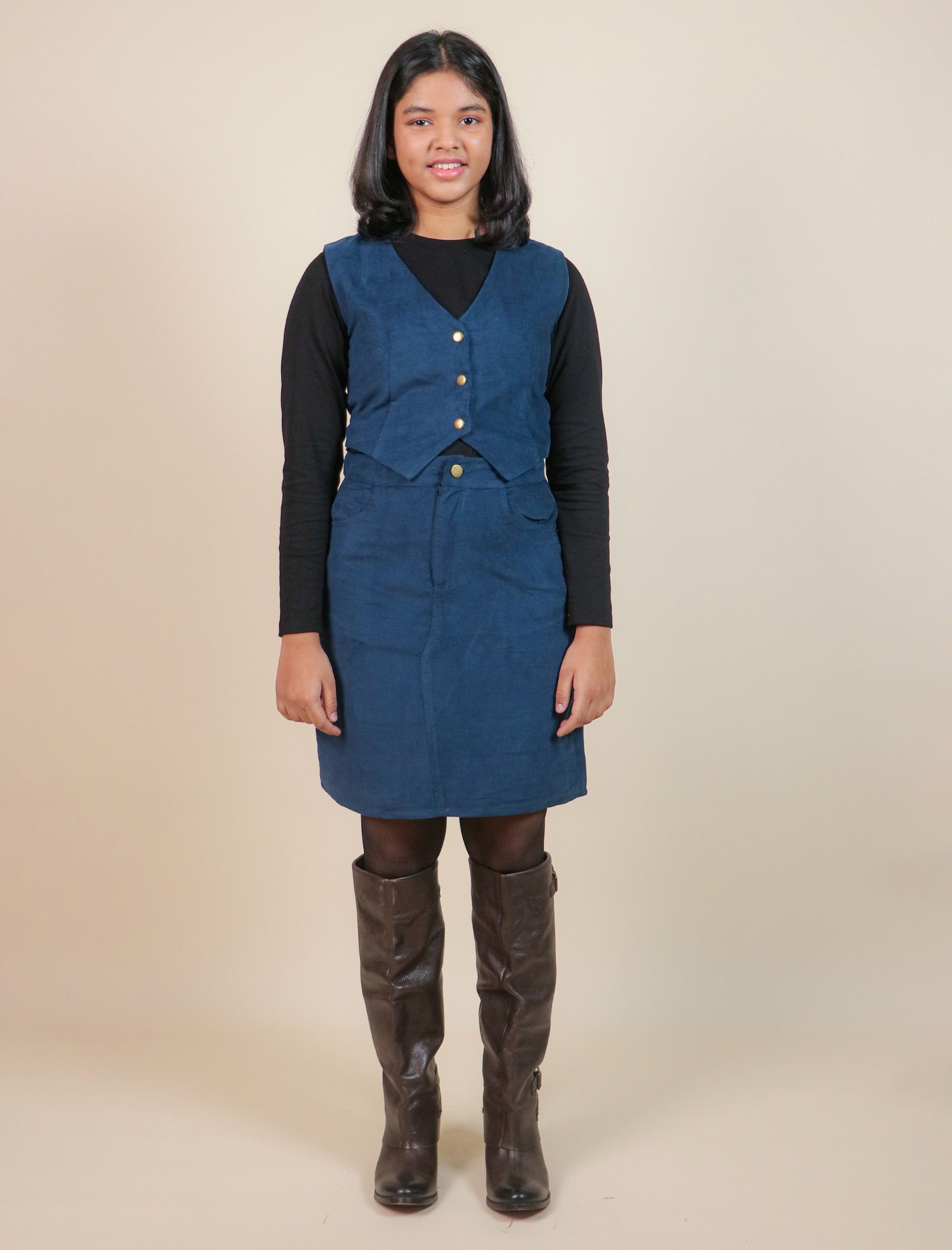 Girls wearing a blue vest over a black shirt with brown boots on a beige background