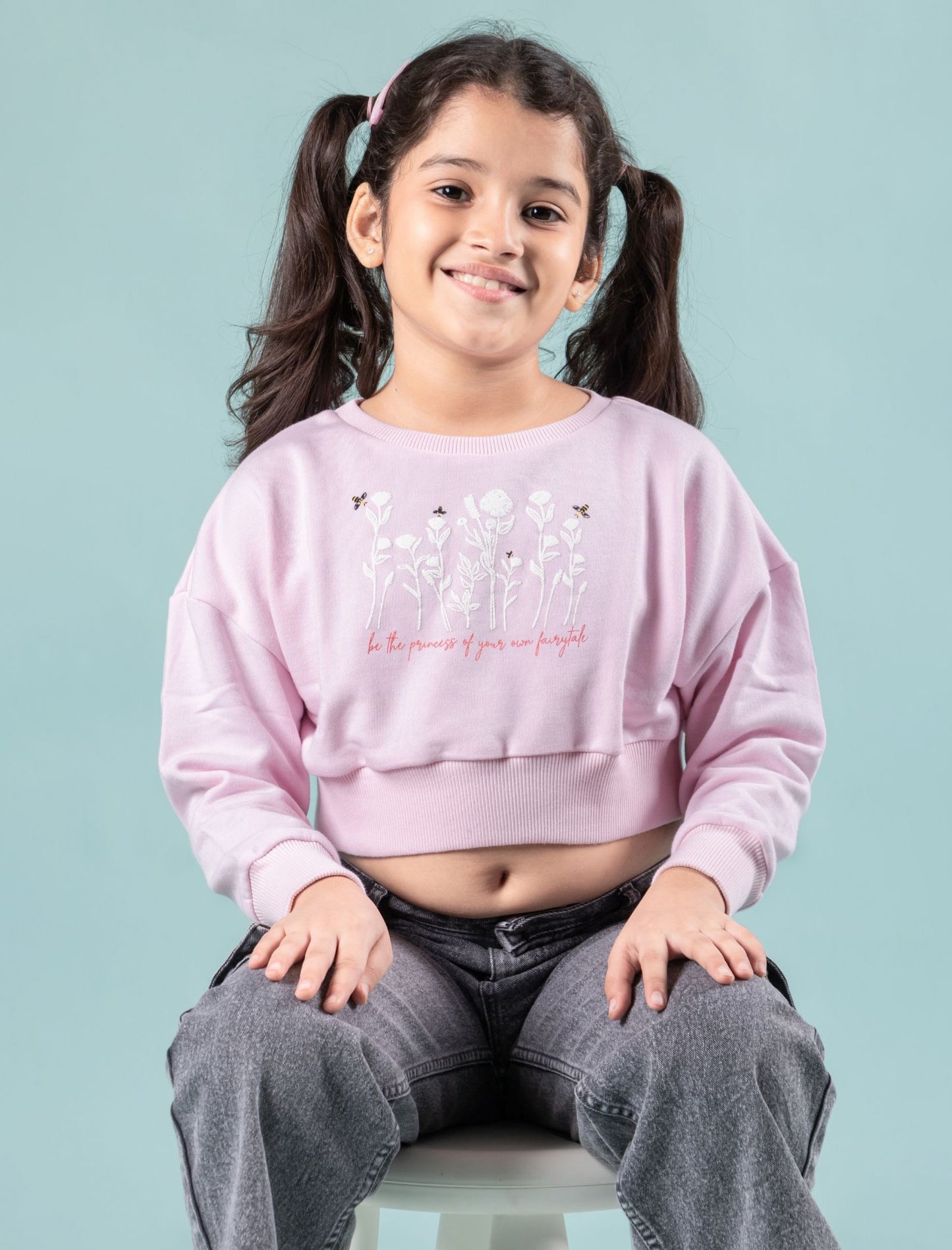 Girls wearing a winter sweatshirt pink colour with text, sitting on a light blue background