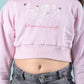 Girls wearing a light pink cropped sweatshirt with floral design and text against a teal background