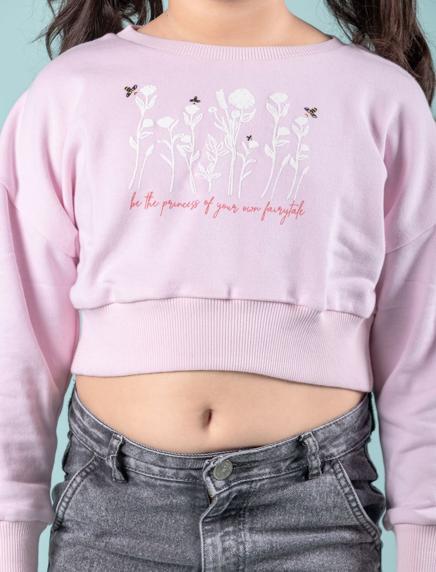 Girls wearing a light pink cropped sweatshirt with floral design and text against a teal background