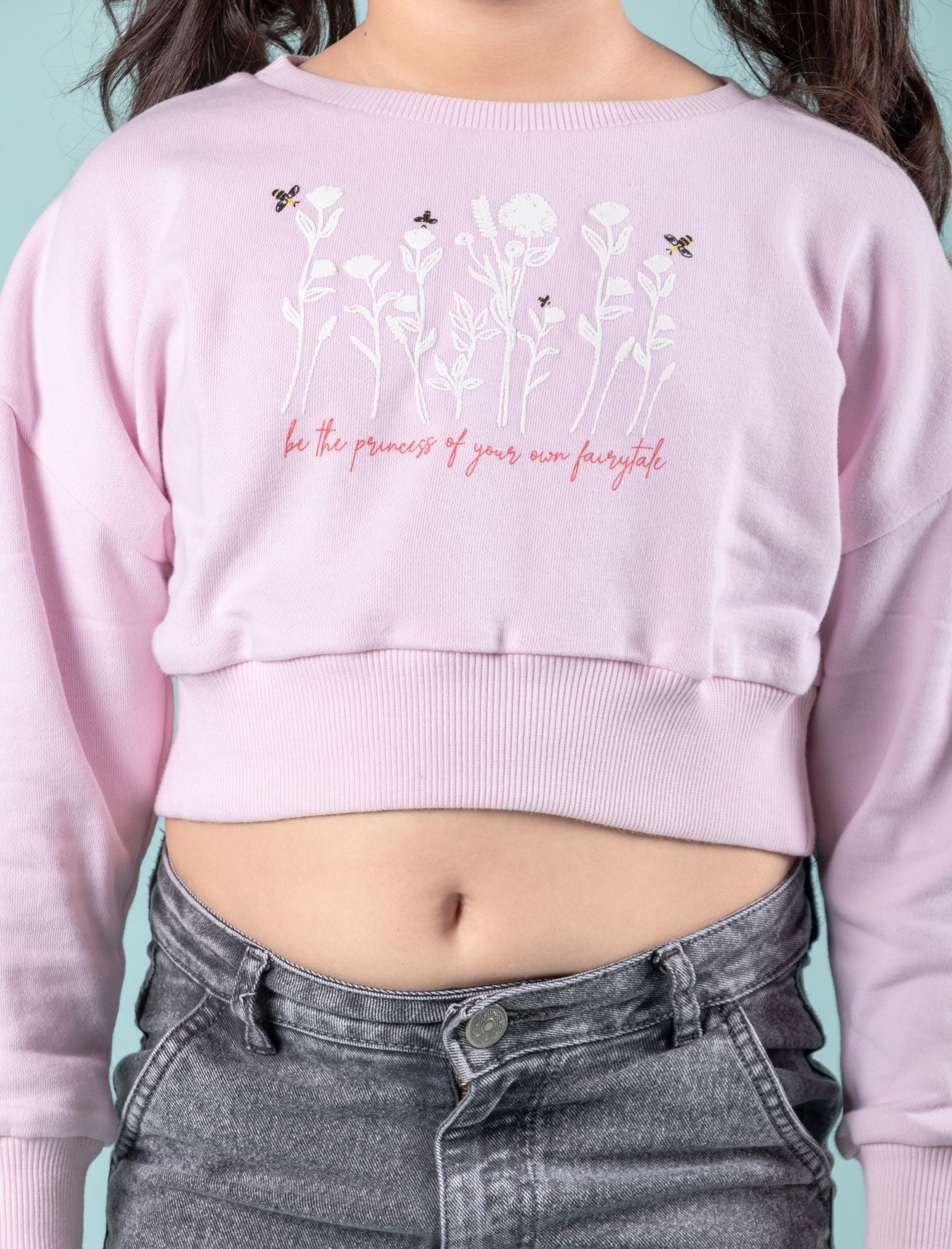 Girls wearing a light pink cropped sweatshirt with floral design and text against a teal background