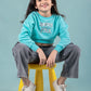 Kids wearing a turquoise sweatshirt with text, sitting on a yellow stool against a light blue background
