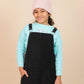 girls wearing a black pinafore dress over a light blue long-sleeve shirt with a pink beanie on a beige background