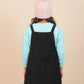 Girls wearing a black pinafore dress over a light blue long-sleeve shirt with a pink knit hat on a beige background