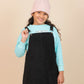 girls wearing a black pinafore dress over a light blue sweater with a pink beanie on a beige background
