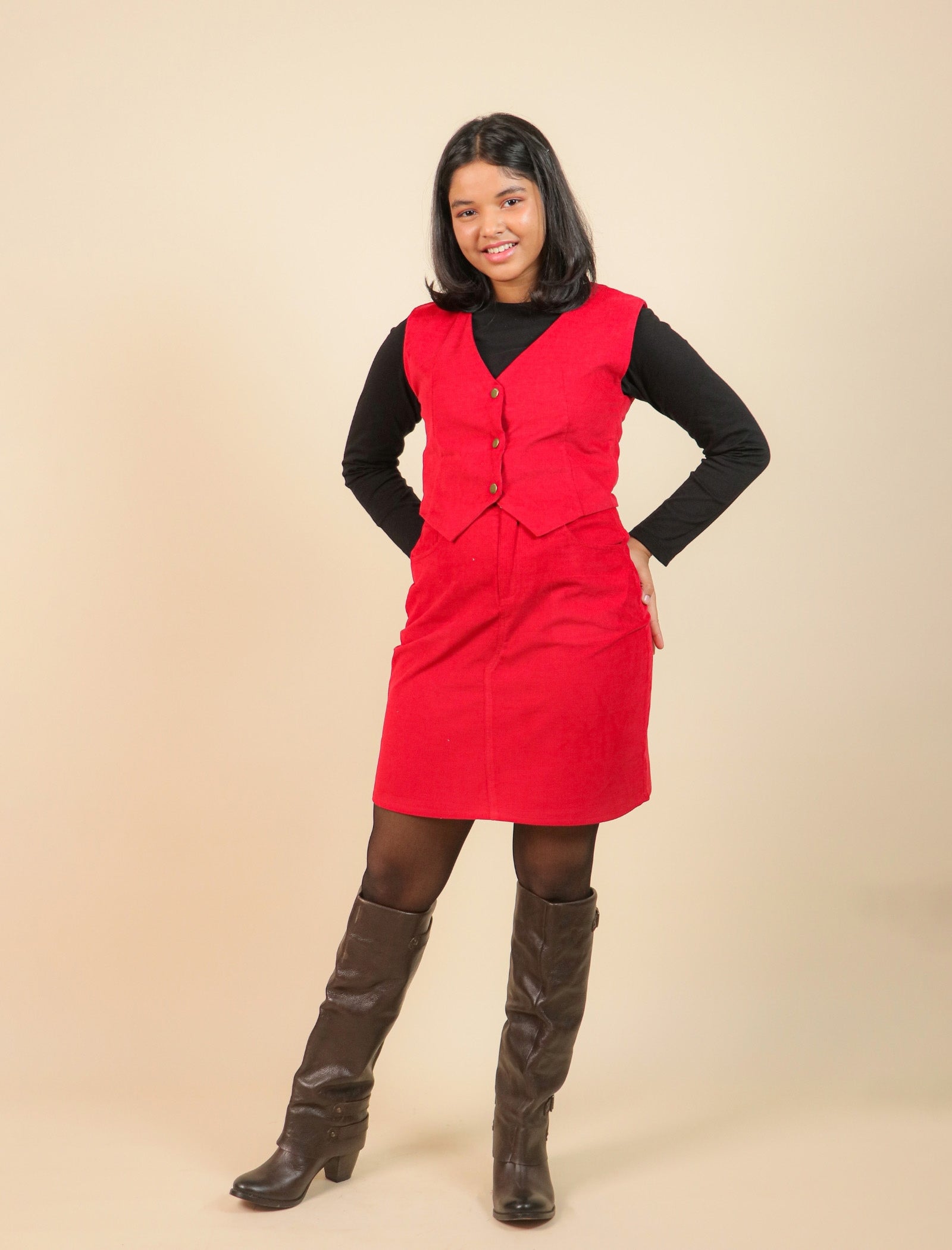 Girls wearing a red dress over a black shirt with brown knee-high boots on a beige background