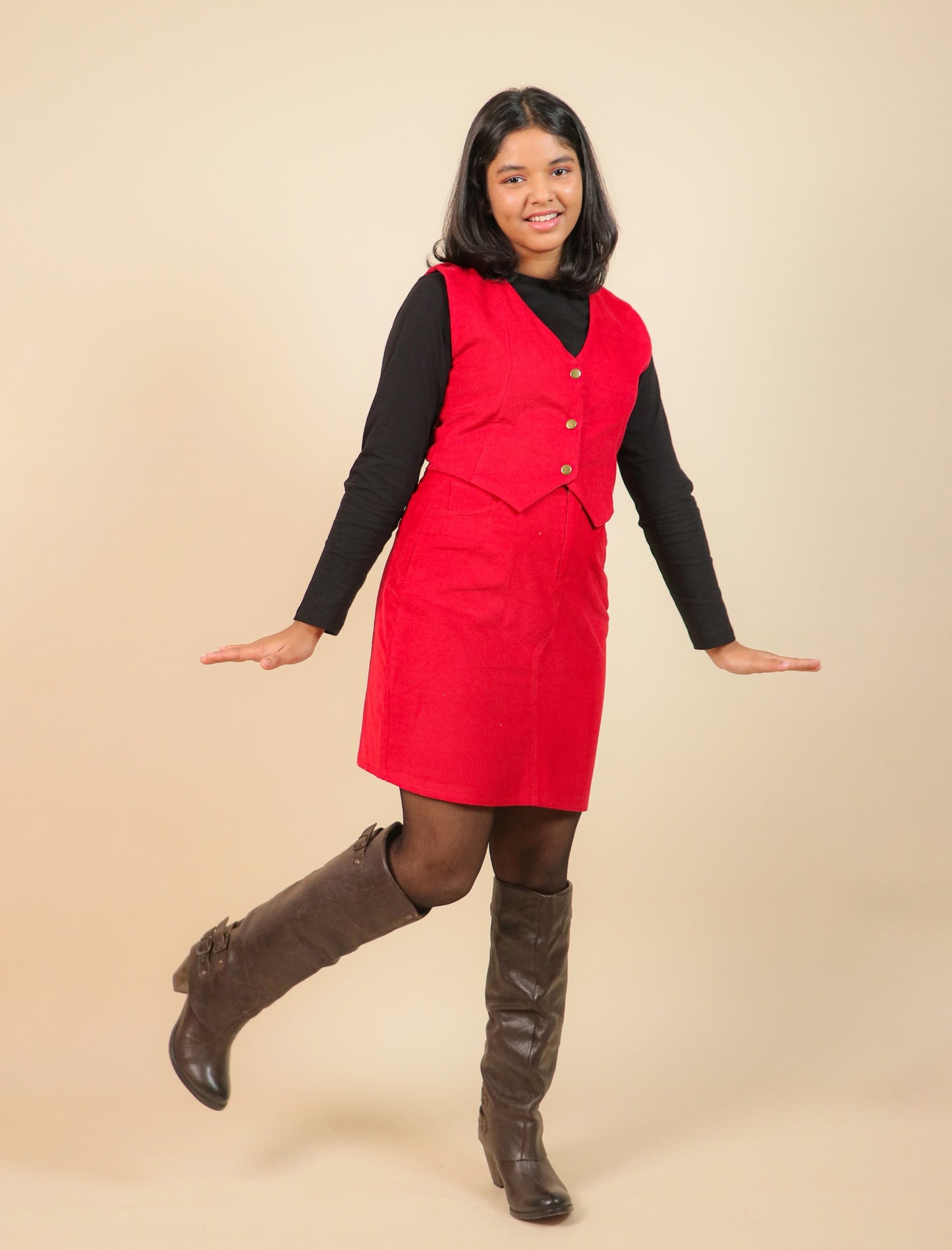 Girls wearing a red dress with a black top and brown knee-high boots on a beige background